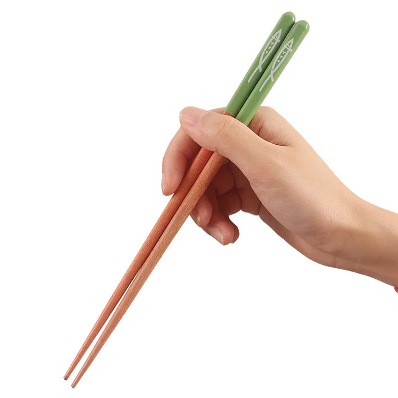 Wooden chopsticks with green handles being held in a hand.