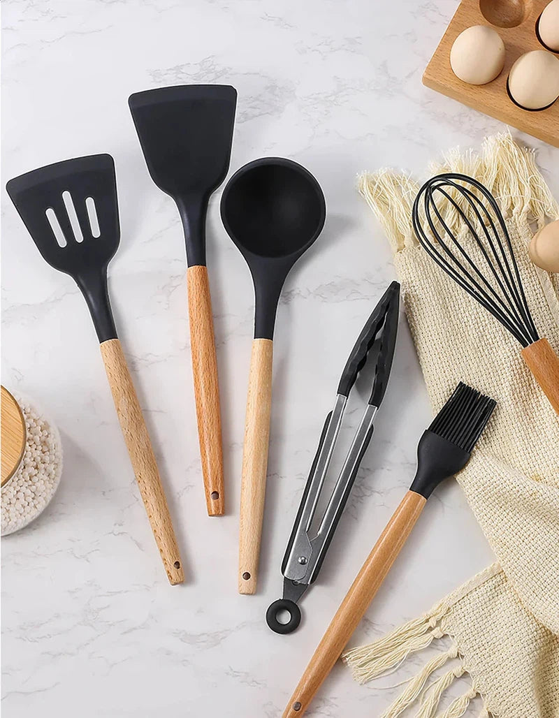 12Pcs silicone kitchen utensils with wooden handles, including spatula, spoon, tong, whisk, and brush on a kitchen counter.