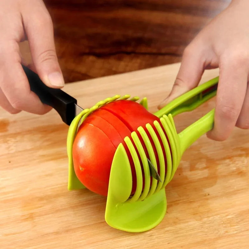 Stainless steel handheld fruit slicer cutting a tomato on a wooden surface.