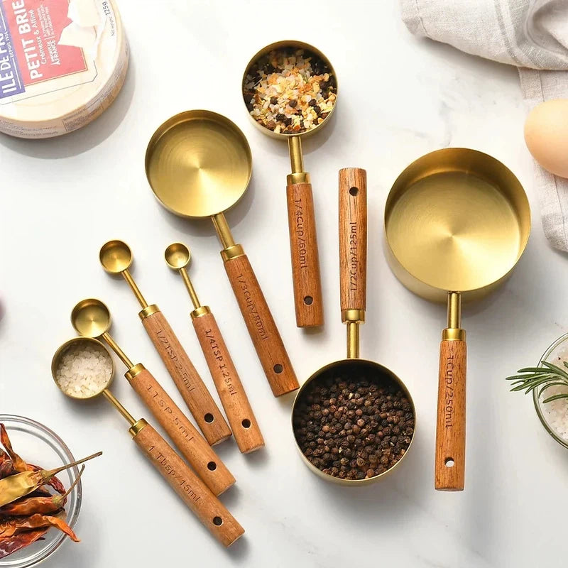 8-piece stainless steel measuring cups and spoons set with wooden handles on a white surface, used for baking and bartending.