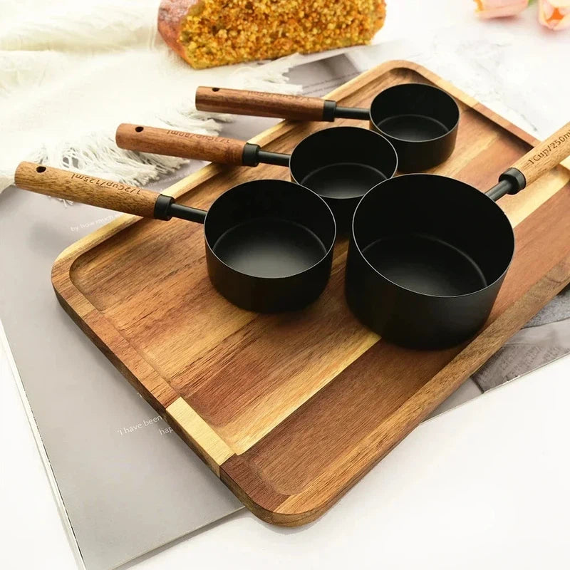 8-piece stainless steel measuring cups set with wooden handles on a wooden tray, suitable for baking and bartending.