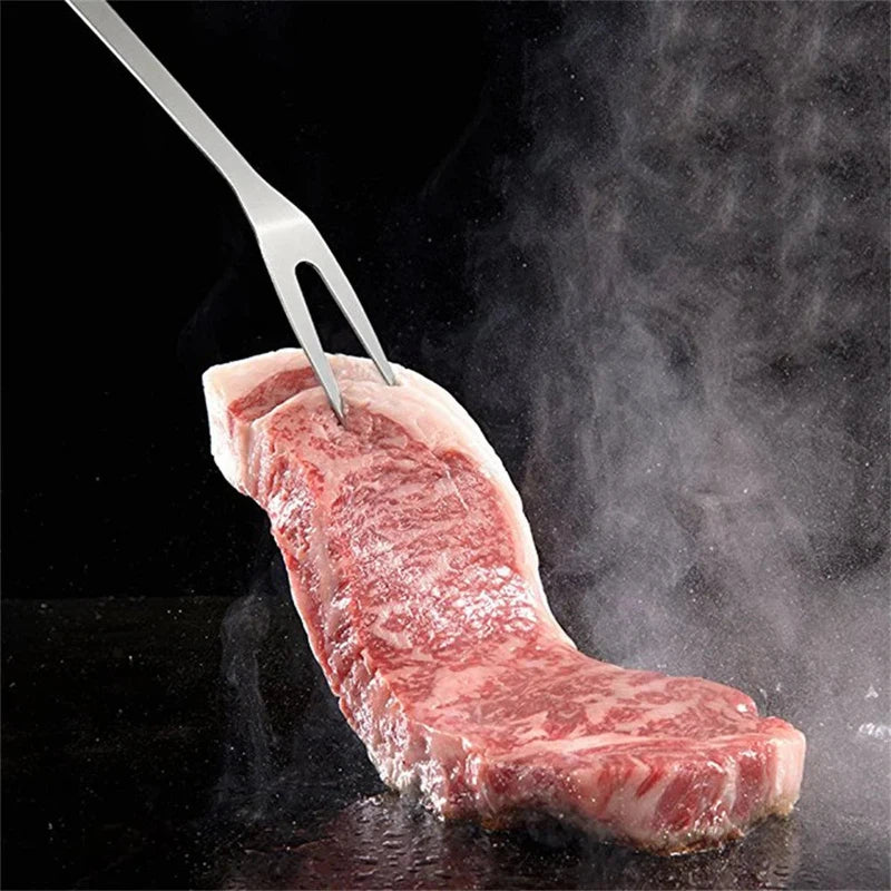 Stainless steel barbecue fork holding a juicy steak on a grill.