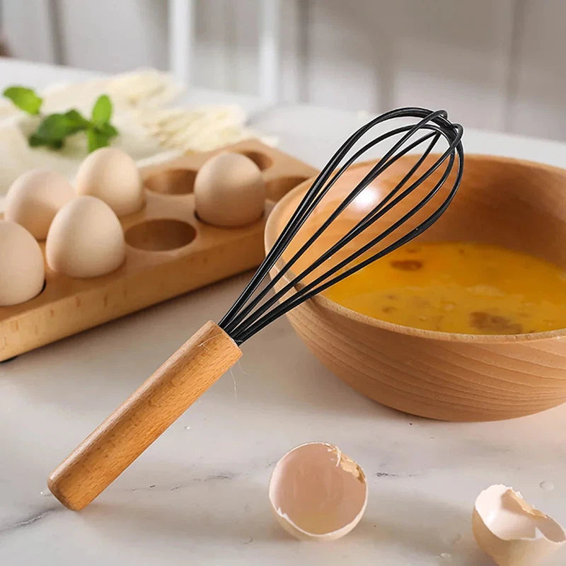 Silicone whisk with wooden handle beside eggs and bowl.