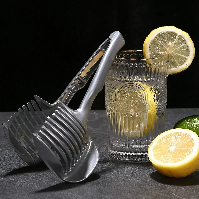 Stainless steel handheld slicer for oranges, lemons, and tomatoes with glass and sliced fruit.